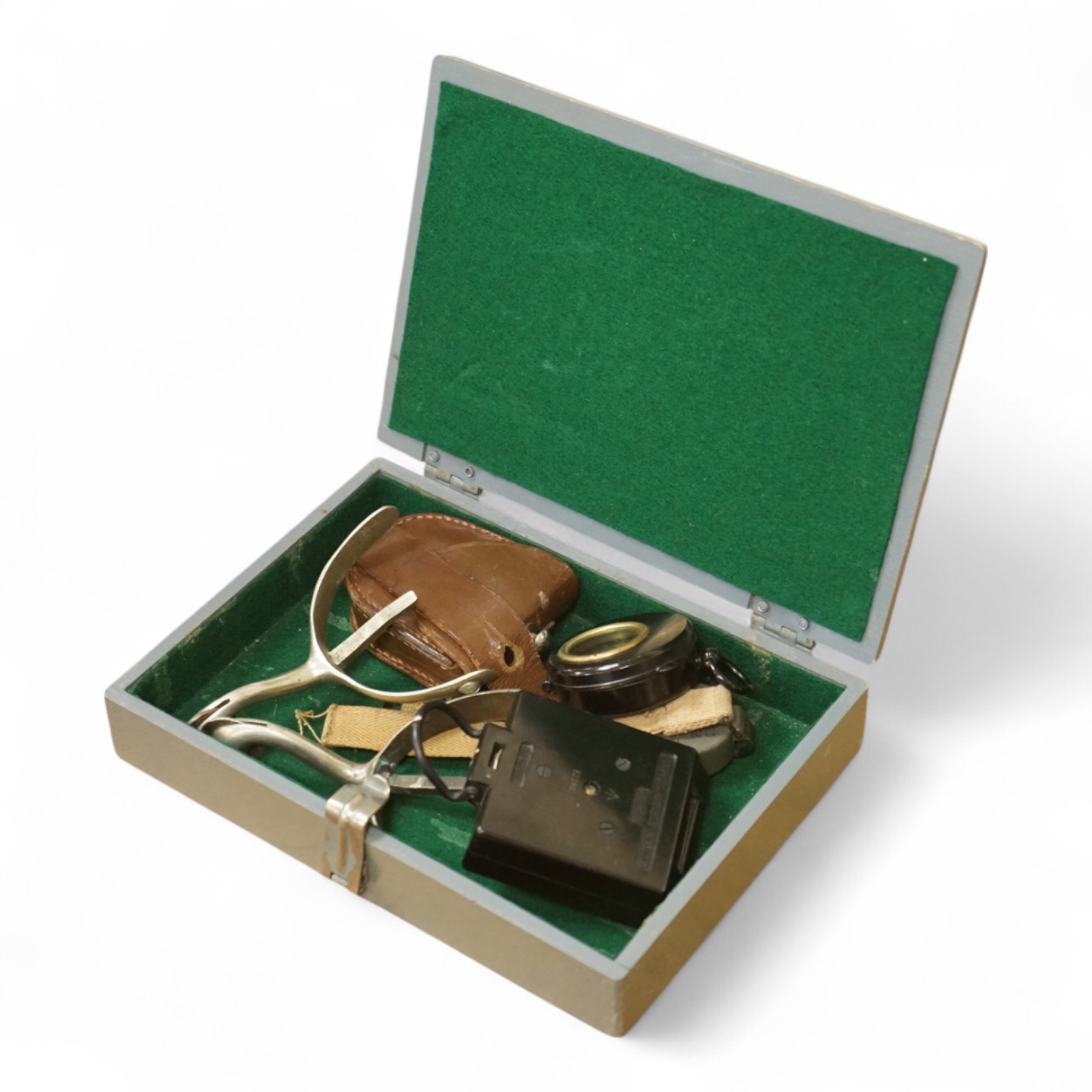 Three WWII military compasses including a Magnetic Marching Mark One compass, a small compass on a wrist strap and another in a leather case, together with a pair of steel spurs and a small grey painted wooden military b